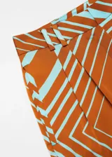Pantalón de tiro medio con diseño recto y fluido, confeccionado en tejido satinado con estampado geométrico en tonos marrón y turquesa. Cuenta con cierre oculto de botón, gancho y cremallera, trabillas para cinturón, pinzas delanteras y dos bolsillos laterales.