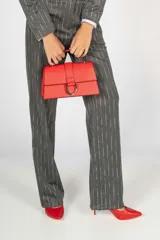 Cartera de mano color beige con solapa frontal y cierre metálico en forma de D. Incluye asa superior y correa ajustable.