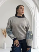 Sweater gris de punto con cuello redondo azul marino y mangas largas con apliques de denim y bolsillos con botón.