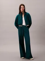 Campera tipo track Calvin Klein de tejido plano en color verde oscuro, de corte cropped y manga larga. Cuenta con cuello alto, cierre frontal de cremallera metálica, bolsillos laterales y elástico acanalado a rayas en los puños y el dobladillo. Presenta el logo de la marca bordado en el pecho.