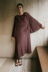 Vestido midi de viscosa color marrón, con cuello redondo, mangas largas amplias y diseño holgado. Presenta bordados en relieve con aplicación de abalorios a tono en el frente.