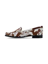 Mocasín de cuero estilo animal print con estampado de vaca en tonos marrón y blanco, con detalle de antifaz en el empeine y suela plana con pequeño tacón.