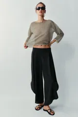 Pantalón fluido de tiro alto en color blanco, con pinzas delanteras, cintura elástica en la espalda y perneras anchas con aberturas laterales pronunciadas.
