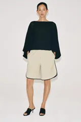 Cuerpo de punto negro con cuello barco, sisa ancha y mangas largas amplias con puños ajustados.