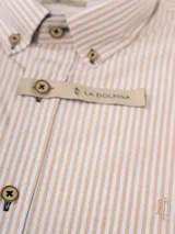 Camisa de manga larga con diseño de rayas verticales en color beige y blanco. Presenta cuello abotonado, cierre frontal con botones y logo de la marca bordado en el pecho.