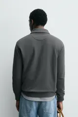 Polo de manga larga color gris oscuro, con diseño de textura estructurada, cuello solapa y cierre frontal de cremallera corta. Cuenta con puños y cintura de rib elástico.