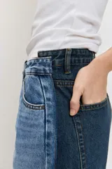 Jean wide leg de tiro medio, confeccionado en denim azul con detalles de paneles laterales en un tono más oscuro, tiro medio, cierre frontal con botón y cremallera, y diseño de perneras amplias.