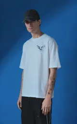 Remera blanca de corte oversize con cuello redondo y manga corta. Presenta una estampa gráfica en la espalda con diseño de palomas, flores y texto en español.