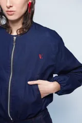 Campera tipo bomber de gabardina de jean color azul oscuro, con cuello a la base, cierre frontal metálico y bolsillos ojal. Presenta mangas largas abullonadas con puños elásticos y costuras con pespuntes en color rojo.