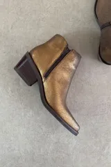 Botín Indiana de cuero vacuno con acabado metalizado dorado, diseño de caña baja, taco cuadrado y punta fina.