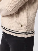Sweater de tejido grueso en color beige, con cuello alto y cierre frontal parcial. Presenta detalles de rayas negras en contraste en el borde del cuello y en los puños.
