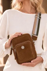 Bandolera pocket bag de cuero vacuno color suela, con bolsillo frontal con cierre y detalle de placa metálica con logo. Cuenta con correa de cinta ancha regulable y herrajes metálicos plateados.