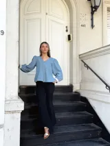 Camisa celeste de jean con cuello en V, mangas largas abullonadas con puños de encaje y cierre frontal con botones.