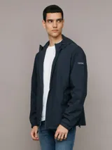 Campera rompeviento Calvin Klein de color azul marino, con cierre frontal de cremallera, capucha ajustable y bolsillos laterales. Presenta un parche con el logo de la marca en la manga y puños elásticos.