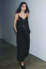 Top negro de viscosa con escote pico y tirantes finos. Presenta un aplique de encaje negro con diseño ornamental en el centro del pecho.