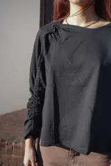 Remera negra de mangas largas con detalle de frunce en una manga y drapeado en el hombro.