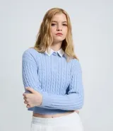 Buzo cropped de punto con textura trenzada, color celeste, con cuello polo camisero en contraste color blanco y cierre frontal con botones. Presenta mangas largas con puños acanalados y ruedo también acanalado.