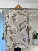 Camisa de lino con estampado batik en tonos beige y marrón, cuello en V con solapa corta y tres botones frontales, y mangas largas.