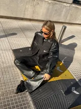 Pantalon negro de tiro alto con diseño combinado, presentando paneles de denim en la parte superior y paneles de cuero sintetico en la parte inferior, con corte recto y ligeramente acampanado.
