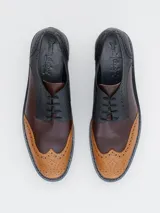 Zapato estilo brogue con plataforma y taco ancho, confeccionado en cuero bicolor con detalles perforados en la puntera y los laterales.