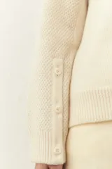 Cárdigan color crema de tejido de punto industrial con escote en V, combinación de puntos y botones decorativos en las mangas.