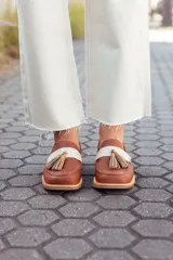 Mocasines de cuero color tostado, con detalle de antifaz en cuero crudo y borlas decorativas. Hechos a mano en Uruguay.