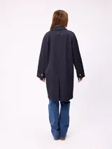Gabardina de corte clásico en color azul marino, con cierre frontal de botones, cuello camisero y bolsillos laterales. Presenta un diseño minimalista con un pequeño bordado en el pecho.