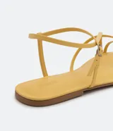 Sandalia plana de mujer color amarillo mostaza, con tiras finas que cruzan sobre el empeine y una tira con hebilla ajustable alrededor del tobillo.
