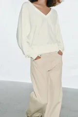 Jersey de punto color blanco crema, con escote en pico, manga larga y sisa ancha terminada en puño.