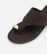 Sandalia plana Satinato confeccionada en cuero color marrón, con diseño de tira para el dedo y detalle metálico dorado redondo. Cuenta con suela baja.