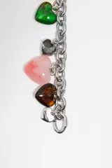 Pulsera de eslabones plateados con dijes colgantes en forma de corazón de diferentes colores, incluyendo amarillo, verde, gris, rosado y marrón.
