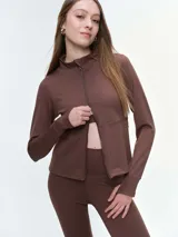 Campera deportiva de cuello alto con cierre frontal de doble cursor. Presenta un corte ajustado que realza la silueta, bolsillos laterales con cierre y mangas largas con puños con abertura para el pulgar.