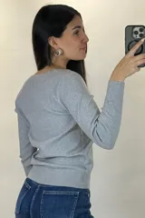 Buzo de hilo gris con textura acanalada, escote en V y cierre frontal con botones pequeños.