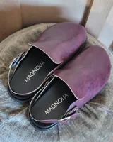 Zuecos de cuero vegano en color bordó con acabado texturizado. Presentan un diseño de punta cerrada con una tira ajustable con hebilla metálica que puede usarse en el tobillo o sobre el empeine.