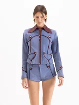 Chaqueta de gamuza color celeste con cuello camisero y detalles de ribetes en cuero marrón. Cuenta con cierre frontal y bolsillos aplicados con solapa.