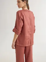 Chaqueta de lino color azul lavanda, de corte holgado, con escote redondo, cierre frontal con botones y mangas ajustables. Presenta un diseño versátil con bordado en la espalda.
