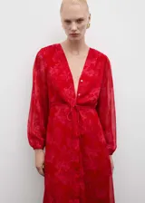 Vestido midi de tejido fluido en color rojo con estampado floral tono sobre tono. Presenta escote en pico, cierre frontal de botones ocultos, mangas largas con puños elásticos y nudo ajustable en la cintura. Incluye forro interior.