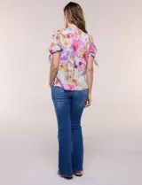 Blusa de gasa liviana con estampado floral en tonos violeta y rosado, cuello redondo y mangas cortas con detalle de lazo en los puños.
