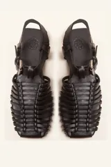 Sandalias planas tipo huarache de cuero negro, con tiras entrelazadas a mano y tira ajustable en el talón con hebilla metálica.