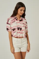 Camisa de corte cropped y manga corta con cuello camisero y cierre frontal de botones. Presenta un estampado abstracto tipo mármol en tonos rosados y negros, con dos bolsillos frontales.