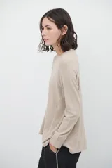 Remera de manga larga en color beige, confeccionada en tejido de punto con costuras a la vista en contraste. Presenta un corte holgado, cuello redondo y un pequeño bordado distintivo en la parte inferior.