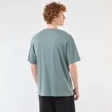 Remera de algodón de corte holgado, color azul grisáceo, con cuello redondo y mangas cortas. Presenta una pequeña etiqueta decorativa en el ruedo inferior.