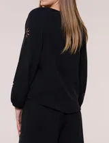 Blusa azul de corte holgado y fluido, con escote en V y mangas largas raglán que presentan detalles de calados con forma de flores y puños elastizados.