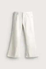 Jeans flare fit color blanco, ajustados en la parte superior y abiertos en campana desde la rodilla, de tiro medio con cinco bolsillos, cierre frontal con cremallera y botón y bajo con acabado irregular.