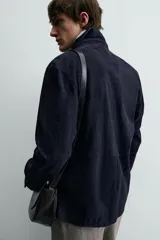 Sobrecamisa de hombre, color azul marino oscuro, confeccionada en piel con acabado ante. Presenta cuello solapa, manga larga con puños abotonados, un bolsillo de parche en el pecho y cierre frontal de botones.