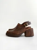 Zapato tipo zueco de cuero color chocolate con efecto desgastado, plataforma y taco cuadrado. Presenta una tira trasera ajustable con hebilla metálica.