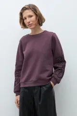 Sweatshirt color ciruela de cuello redondo y manga larga, con detalle de apliques bordados en relieve en las mangas.