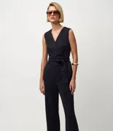 Mono largo sin mangas, confeccionado en tejido Ponto Roma de viscosa certificada, con estampado de rayas verticales finas. Presenta un diseño cruzado en el torso con lazo ajustable a la cintura y pantalón de pierna ancha.