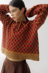 Buzo de tejido de punto con diseño de rombos en tonos beige y marrón. Presenta cuello polo con cierre frontal de tres botones, mangas largas con puños acanalados y ruedo también acanalado.