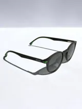 Lentes de sol con armazón de diseño redondeado en color negro mate y detalles en verde vibrante en las bisagras y el interior de las patillas. Cuentan con cristales oscuros polarizados y protección UV 400.